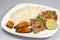 A steak covered in pico de gallo surrounded by plantains and white rice on a white plate. Cuban food.