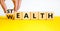 Stealth wealth symbol. Businessman turns the wooden cube and changes the word `wealth` to `stealth`. Beautiful yellow table, w