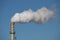 Steam comes out a chimney above a factory with white steam cloud on clear blue sky in Rotterdam.