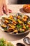 Steam cooked mussels with Vinaigrette garnish on beige plate, top view, Mediterranean cuisine.