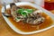 steam fried Marbled Goby fish called Ikan Malas in siamese style served in a dish on a wooden table in a restaurant in Indonesia