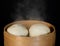 Steam rising from cooked buns in bamboo steamer basket