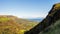 A steam side of a mountain and vast valley below with cliffs and sea from in a distance, autumn landscape with blue sky and clouds