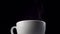 Steam from a white cup evaporates and dissolves against a black background.