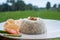 Steamed rice with prawn crackers and vegetables on white plate over blurred rice fields