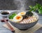 A steaming bowl of ramen noodles topped with slices of tender pork belly, soft-boiled egg