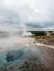 Steaming colorful hot spring pool with Strokkur geyser at the background in Geysir geothermal area