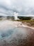 Steaming colorful hot spring pool with Strokkur geyser at the background in Geysir geothermal area