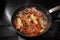 Steaming cooking pan with roasting vegetables like king oyster mushrooms, red peppers and onions on a black stove, copy space