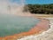 Steaming Rotorua hot springs, New Zealand. Yellow and blue hot springs with steam rising, trees in background.