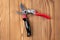 Steel gardening secateurs, scissors tool with red and black grip for pruned of plants and flowers garden work, on a wooden table