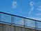 steel guard rail with vertical pickets and posts along highway. blue sky with white clouds. thick concrete slab