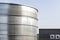 Steel industrial silos for liquids and solids standing in a factory next to a concrete building.