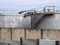 Steel industrial storage tanks with rusty stairs and walkways behind a shabby corrugated iron fence and wall