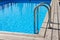 Steel ladder stairs into blue outdoor skimmer pool, wooden floor