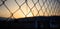 Steel wire mesh fence on a sunset background. Blurred smokestacks and hills silhouette.