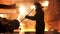 Steel worker removing slag from the electric induction crucible melting furnace at the metallurgical plant, hard work