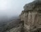 Steep cliffs with a misty gloomy sky. A thick, eerie fog hangs over the mountain and the valley