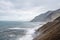 Steep cliffside with volcanic beach and waves crashing to shore.