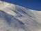 Steep gradient piste in Italian Alps with lone expert snowboarder heading down, against a beautiful blue sky