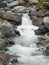 Steep stony stream bed of Alpine brook. Blurred waves of stream running over boulders and stones, high water level after rains