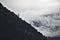 Steep wooded mountain ridge in the Austrian Alps silhouetted against mist and clouds with one protruding pine tree