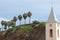 Steeple of the parish church in Camara de Lobos and mound of rock with palm trees