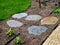 stepping stones lead to a small circular lawn in the middle of a flower bed.