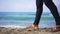 Steps of unrecognizable African American young man in sandals strolling on sandy beach with turquoise blue Mediterranean