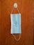 Sterile unused blue face mask hanging from a brown wooden door isolated no people