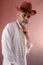 Stern serious elderly man in a white shirt, in a cowboy hat and with a metal chain in his hands