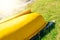 The stern of a yellow plastic boat lying upside down over wooden oar on the grass