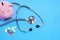 Stethoscope, bunch of pills and piggy bank on blue background