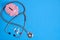 Stethoscope, bunch of pills and piggy bank on blue background