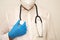 A stethoscope on the chest of a masked doctor and a hand in a blue latex glove