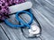 A stethoscope and an electronic thermometer lie on a wooden background next to a bouquet of lilacs. Concept spring and