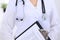 Stethoscope at female doctor breast at hospital office. Unknown physician`s hands close-up. Medicine and health care