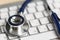 Stethoscope head lying on silver keyboard closeup