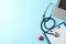 Stethoscope, laptop, tablet, pen and heart on blue background