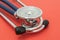 Stethoscope or phonendoscope, with the big chest piece or diaphragm upwards, lying on a red uniform background close up front view