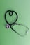 Stethoscope in the shape of heart on green background