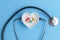 Stethoscope and various pills in a saucer in shape of heart on a blue wooden background