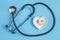 Stethoscope and various pills in a saucer in shape of heart on a blue wooden background