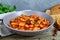 Stewed broad beans in tomato sauce with herbs and spices close-up, slices of rye bread