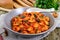 Stewed broad beans in tomato sauce with herbs and spices close-up, slices of rye bread