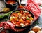 Stewed pepper and sausage with tomatoes in a cast iron skillet on a black background, close up.