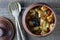 Stewed potato, carrot, onion, tomato and prunes in a clay pot on wooden background, closeup