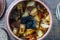 Stewed potato, carrot, onion, tomato and prunes in a clay pot on wooden background, closeup