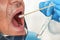 Stick with cotton swab to be inserted into elderly patient open mouth, tube for virus specimen transport held by hand in blue