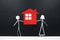 Stick couple figure together holding a red house cutout in black background. Home ownership, housing loan concept.